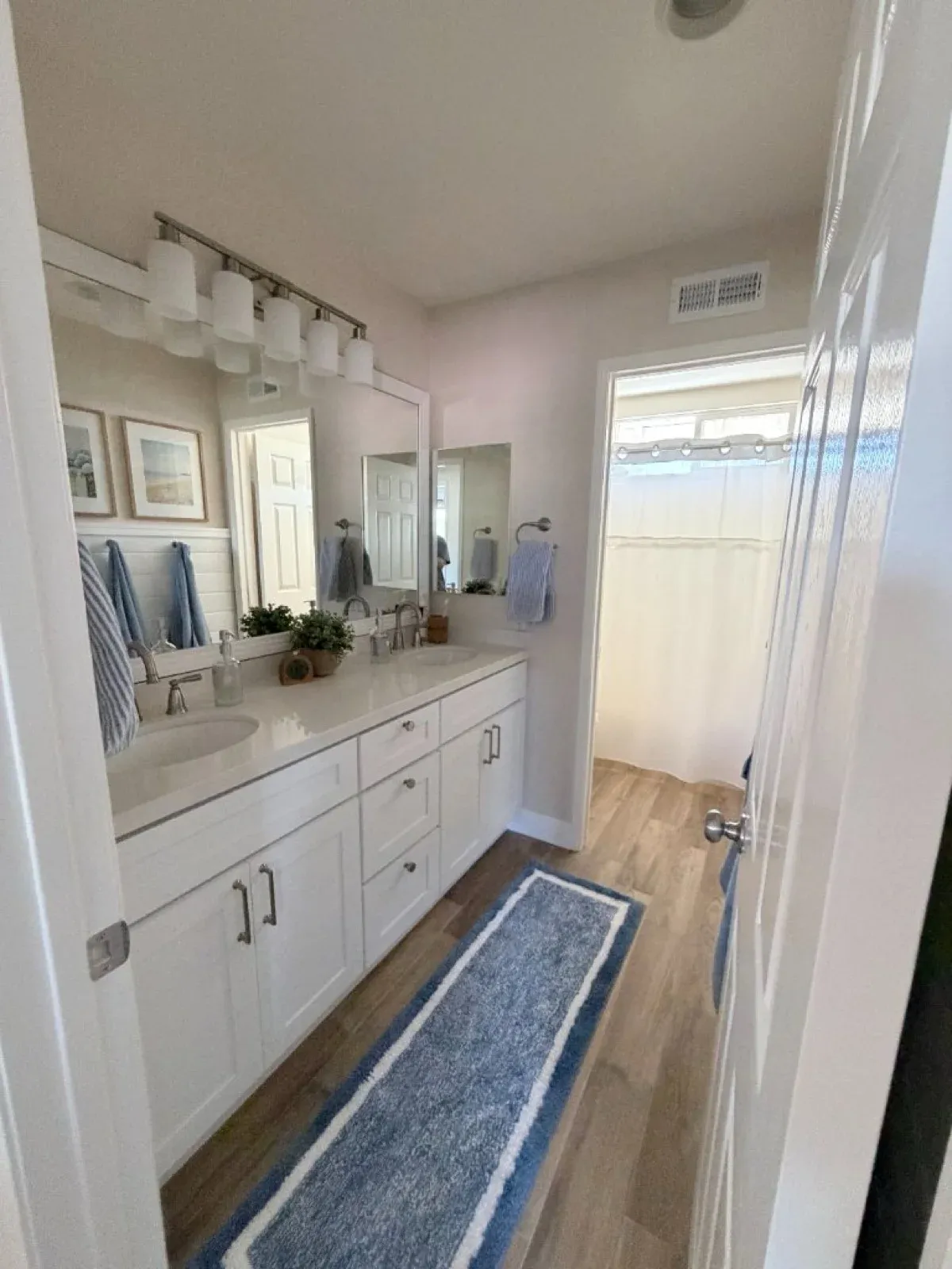 Beautifully restored bathroom with white double vanity, quartz countertop, and wood-look tile flooring after water damage restoration in Murrieta